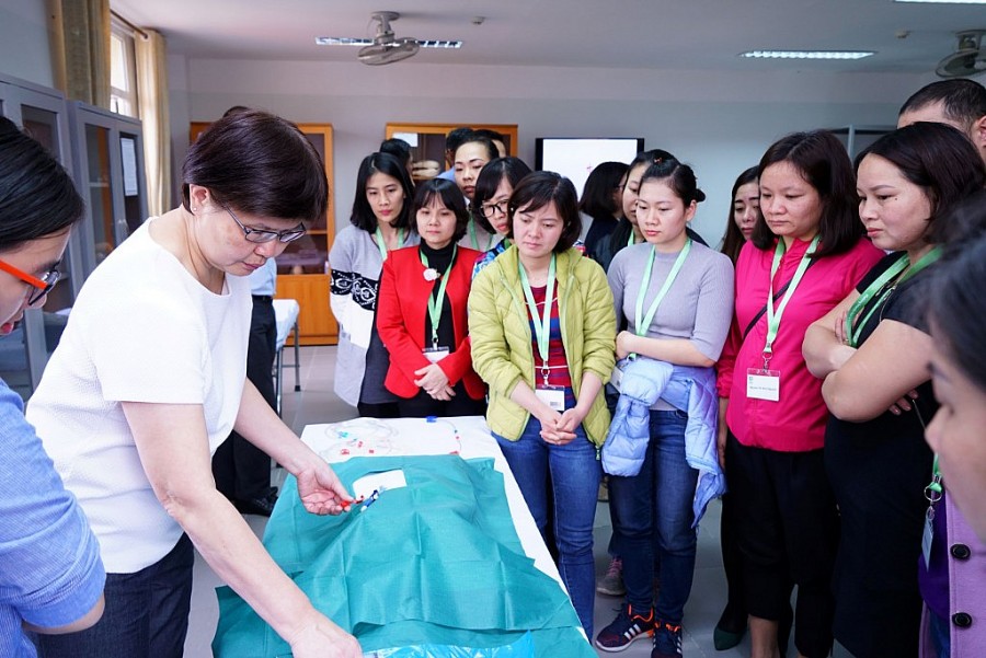 Bà Chan Siew Mie (trái, áo trắng), Tình nguyện viên Quốc tế Singapore và Quản lý y tá cấp cao từ Bệnh viện Tan Tock Seng đang thực hiện kỹ thuật đặt ống thông vĩnh viễn cho các Giảng viên nguồn của Việt Nam trong hội thảo đào tạo lâm sàng năm 2018