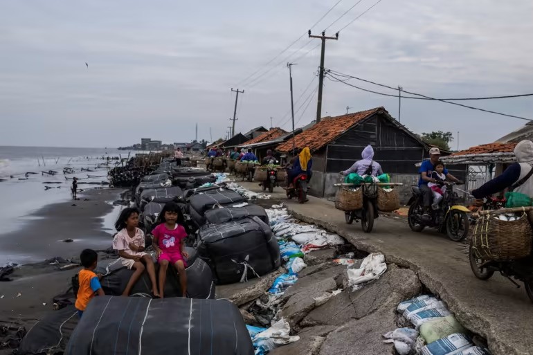 Trẻ em ngồi trên bao cát bên một con đường bị phá hủy bởi sóng cao do mực nước biển dâng cao, ở Cemarajaya vào ngày 3/1.