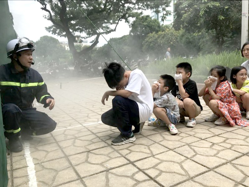 Các em học sinh cùng người dân được hướng dẫn trải nghiệm vượt qua nhà khói, thoát nạn trong không gian hạn chế