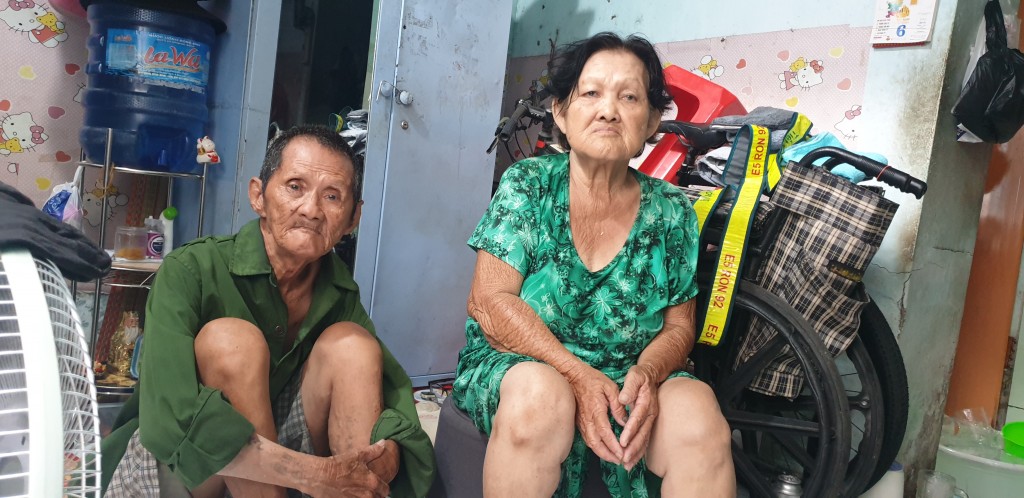 ông Trang Công Quản và bà Nguyễn Thị Nên vưa về nhà sau buổi sàng đi bán. phía sau là chiếc xe lăn phương tiện mưu sinh của ông bà
