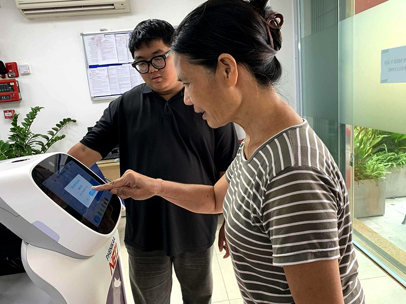 Anh Cao Việt Hà tiếp đón, hướng dẫn bà Trần Thị Hòa bấm lấy số thứ tự trên robot