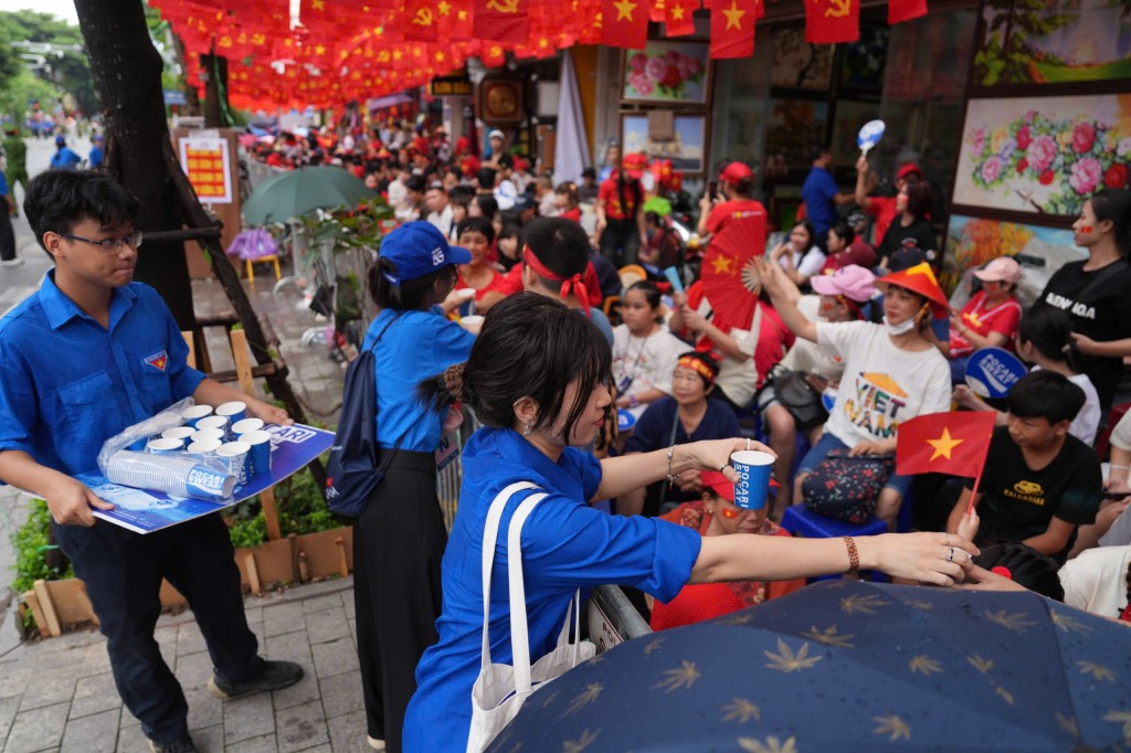 Tình nguyện viên áo xanh mang từng thùng nước len vào dòng người, tiếp sức cho nhân dân trong buổi sơ duyệt diễu binh, diễu hành.
