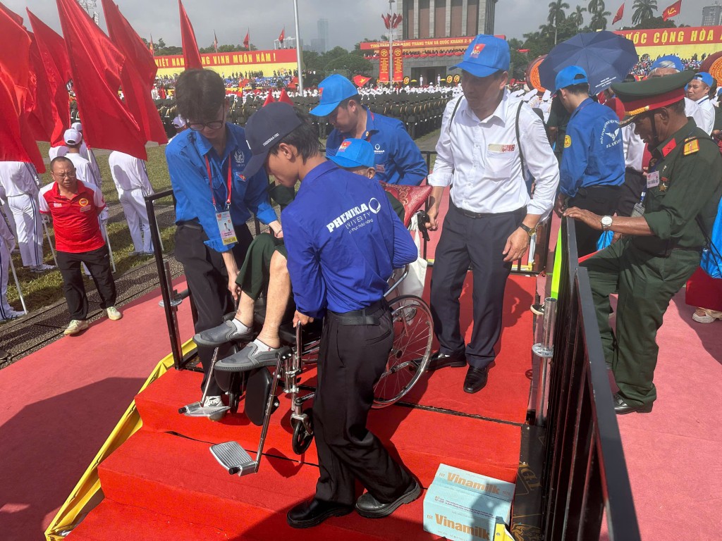 Phối hợp lực lượng chức năng hỗ trợ một đại biểu trên xe lăn qua bậc thềm, bảo đảm an toàn tuyệt đối.