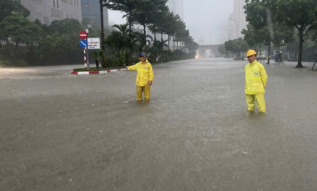 Công nhân Xí nghiệp Thoát nước số 2 ứng trực kết hợp phân luồng giao thông tại điểm ngập trên phố Dương Đình Nghệ. Ảnh: Ngọc Uyên