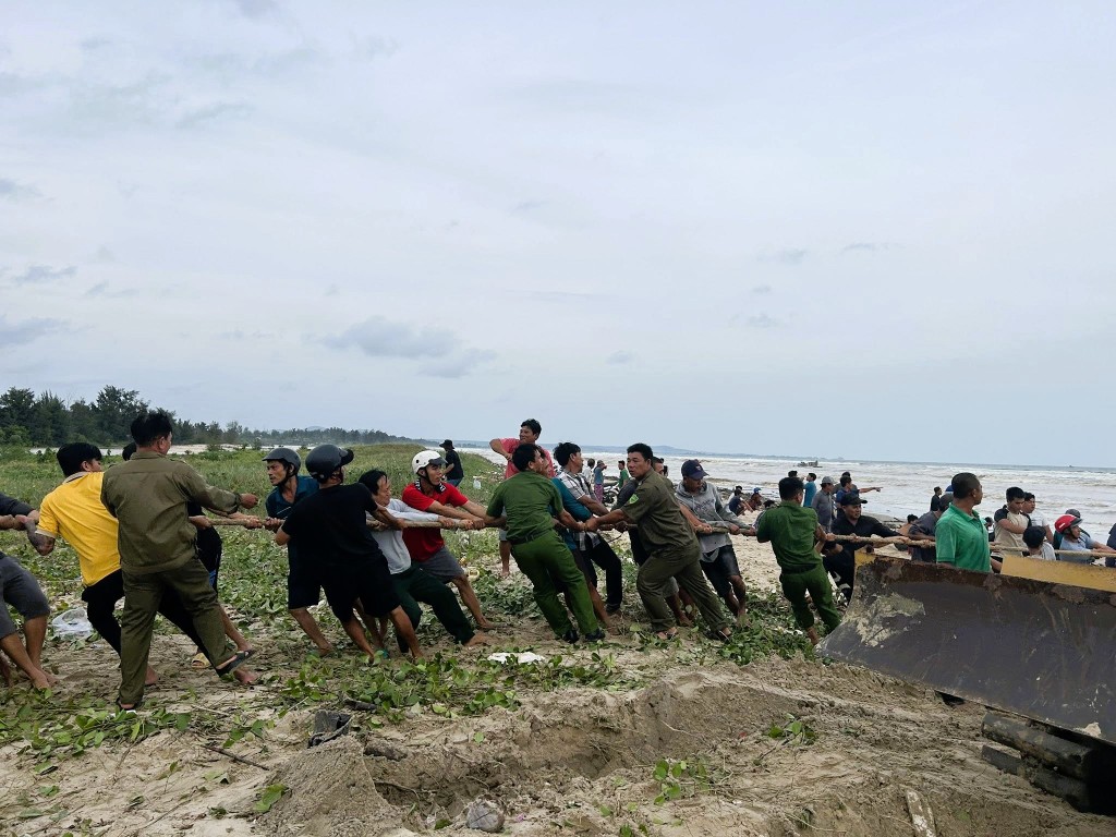 Lực lượng Công an cùng hàng chục người dân hỗ trợ đưa tàu cá lên bờ (Ảnh: CACC)