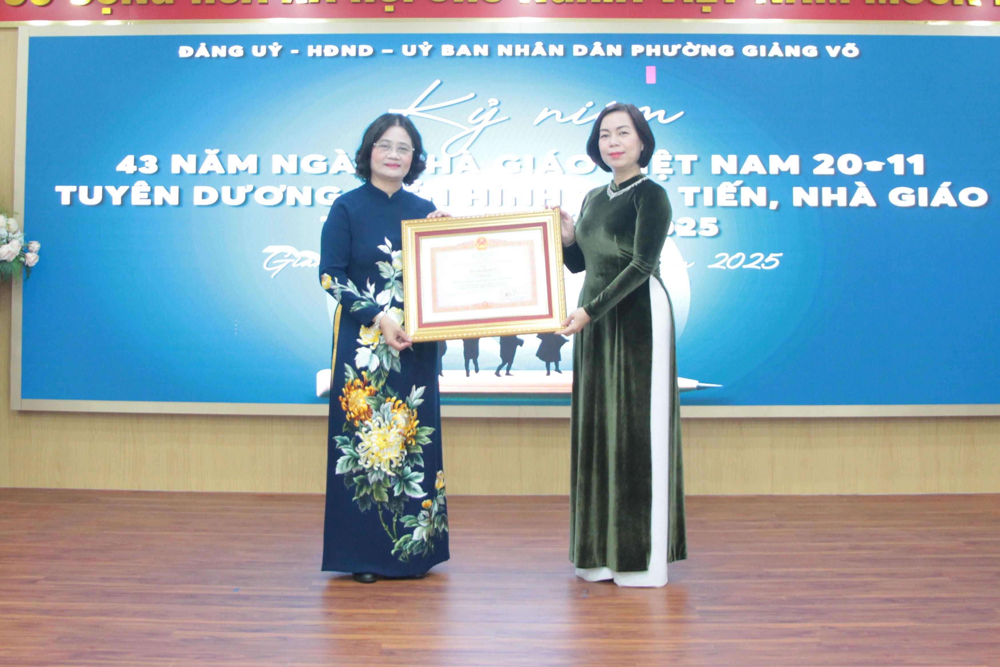 Phó Bí thư Thường trực Đảng ủy phường Giảng Võ Nguyễn Quế Anh (bên phải) trao tặng Bằng khen của Thủ tướng Chính phủ cho Hiệu trưởng Trường THCS Giảng Võ. Ảnh: MH