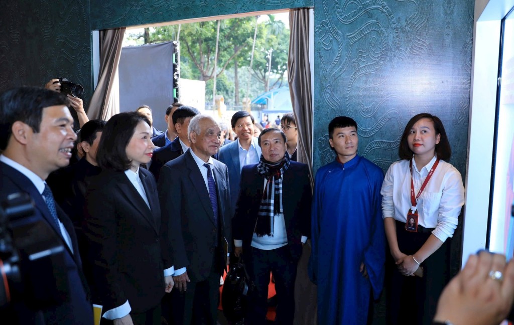 Phó Chủ tịch UBND thành phố Hà Nội và các đại biểu tham quan Không gian trải nghiệm số. Ảnh: Hoàng Lân Bên cạnh vở trình diễn 3D mapping, tâm điểm của chương trình còn nằm ở không gian trải nghiệm đa giác quan Immersive – một hệ sinh thái di sản số được thiết lập ngay trong lòng Hoàng thành Thăng Long. Tại đây, công nghệ không chỉ đóng vai trò minh họa mà trở thành “linh hồn” kết nối quá khứ với hiện tại, biến những tư liệu lịch sử khô khan thành một hành trình cảm xúc sống động, có khả năng chạm tới công chúng ở nhiều lứa tuổi. Không gian trải nghiệm số được tổ chức thành sáu phân khu công nghệ đặc sắc. Khu Visual Mapping 3D tái hiện không gian văn hiến Thăng Long xưa bằng kỹ thuật đồ họa chuyển động kết hợp hệ thống cảm biến thông minh. Những công trình kiến trúc tiêu biểu, cảnh sinh hoạt cung đình, lễ nghi triều chính hiện lên bề thế, sống động cùng hiệu ứng ánh sáng, khói mờ và âm nhạc truyền thống, tạo cảm giác như đang dạo bước trong hoàng cung thế kỷ XI. Khu Holobox 3D ứng dụng công nghệ hologram ánh sáng tiên tiến, cho phép các bảo vật triều Lý như đầu rồng đất nung, mô hình Tháp Báo Thiên, chùa Diên Hựu xuất hiện dưới dạng hình ảnh ba chiều lơ lửng trong không gian thực. Khách tham quan có thể quan sát hiện vật từ nhiều góc độ mà không bị giới hạn bởi lớp kính trưng bày, mang lại trải nghiệm thị giác mới mẻ và ấn tượng. Các nhân vật ảo đại diện cho vua, tăng quan, học sĩ thời Lý cũng được tái hiện sinh động bằng hiệu ứng chuyển động chân thực. al.jpg Khu trải nghiệm Lan tỏa giá trị di sản nghìn năm bằng ngôn ngữ công nghệ hiện đại