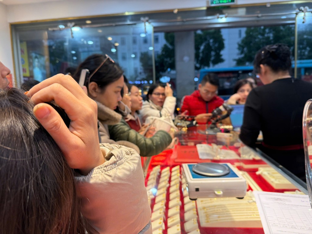 Bên trong cửa hàng vàng, khách chờ giao dịch kín quầy, trong đó có không ít người trẻ tranh thủ theo dõi giá vàng và thực hiện mua – bán ngay trong ngày. Bên trong cửa hàng vàng, khách chờ giao dịch kín quầy, trong đó có không ít người trẻ tranh thủ theo dõi giá vàng và thực hiện mua – bán ngay trong ngày.