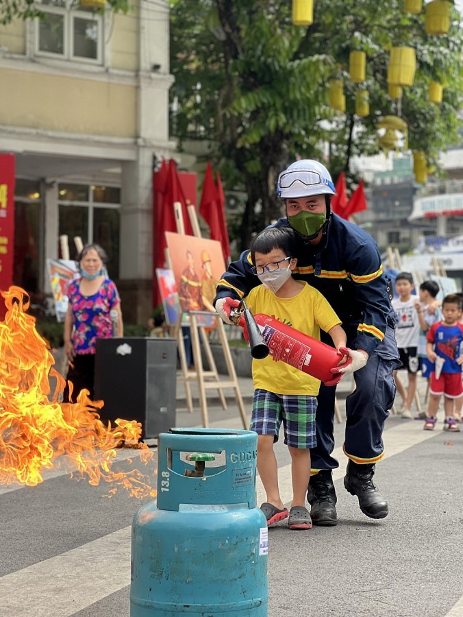 Cán bộ PCCC&CNCH Công an quận Hoàn Kiếm hướng dẫn bạn nhỏ sử dụng bình chữa cháy trong buổi tuyên truyền tại không gian phố đi bộ Hoàn Kiếm