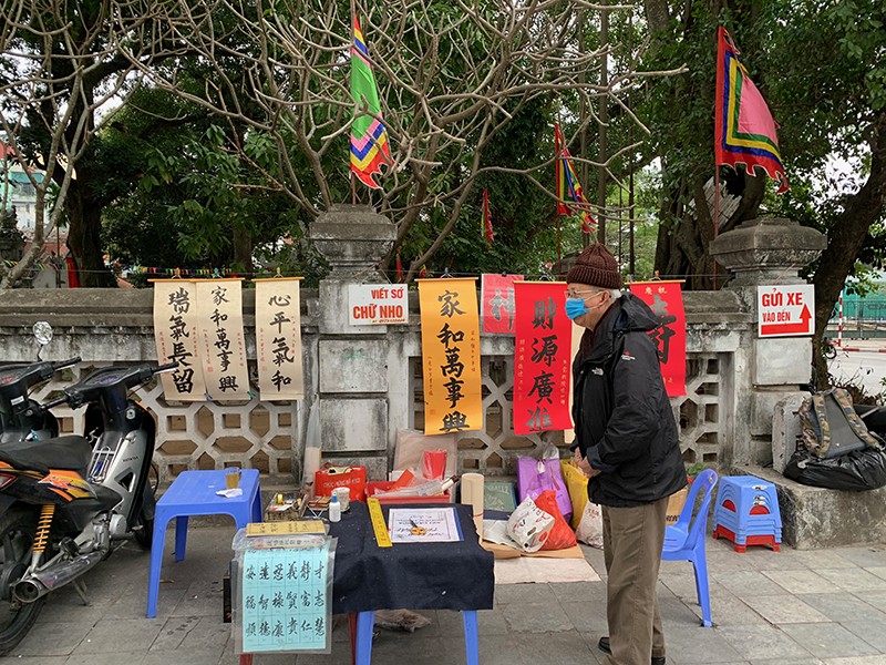 Một cụ ông viết thư pháp đang dọn hàng phục vụ du khách trước cổng đền Quán Thánh Một cụ ông viết thư pháp đang dọn hàng phục vụ du khách trước cổng đền Quán Thánh