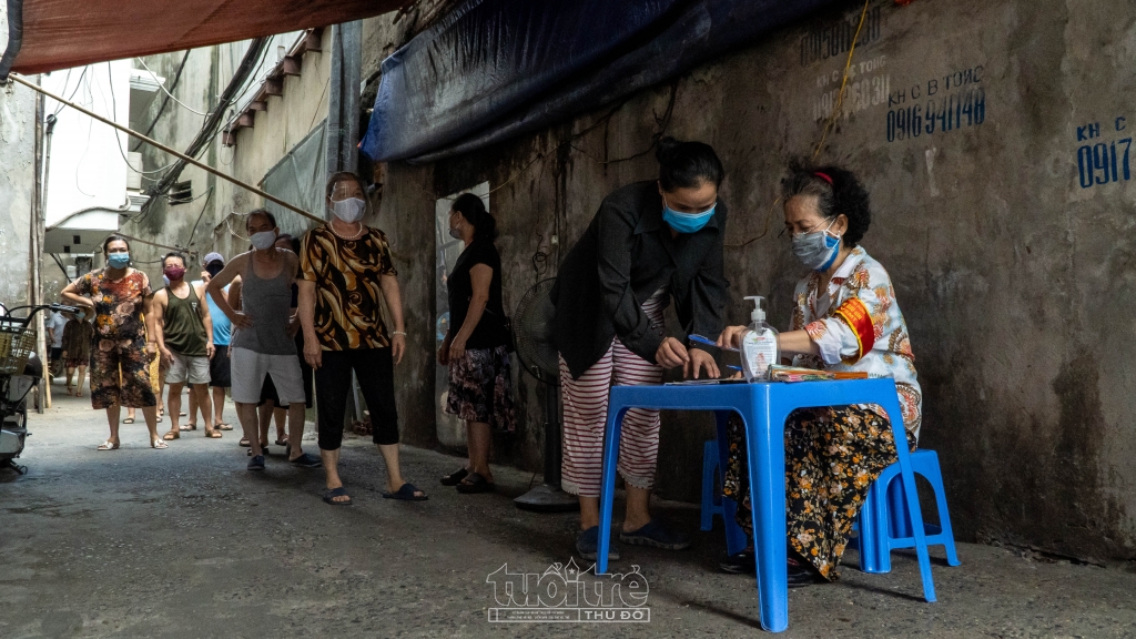 Người dân khi tới nhận hỗ trợ được yêu cầu xếp hàng giãn cách đồng thời sát khuẩn tay trước khi nhận quà