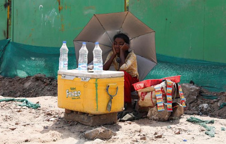 Cô bé bán nước dưới chiếc ô để che nắng ở New Delhi. Ảnh: CNN