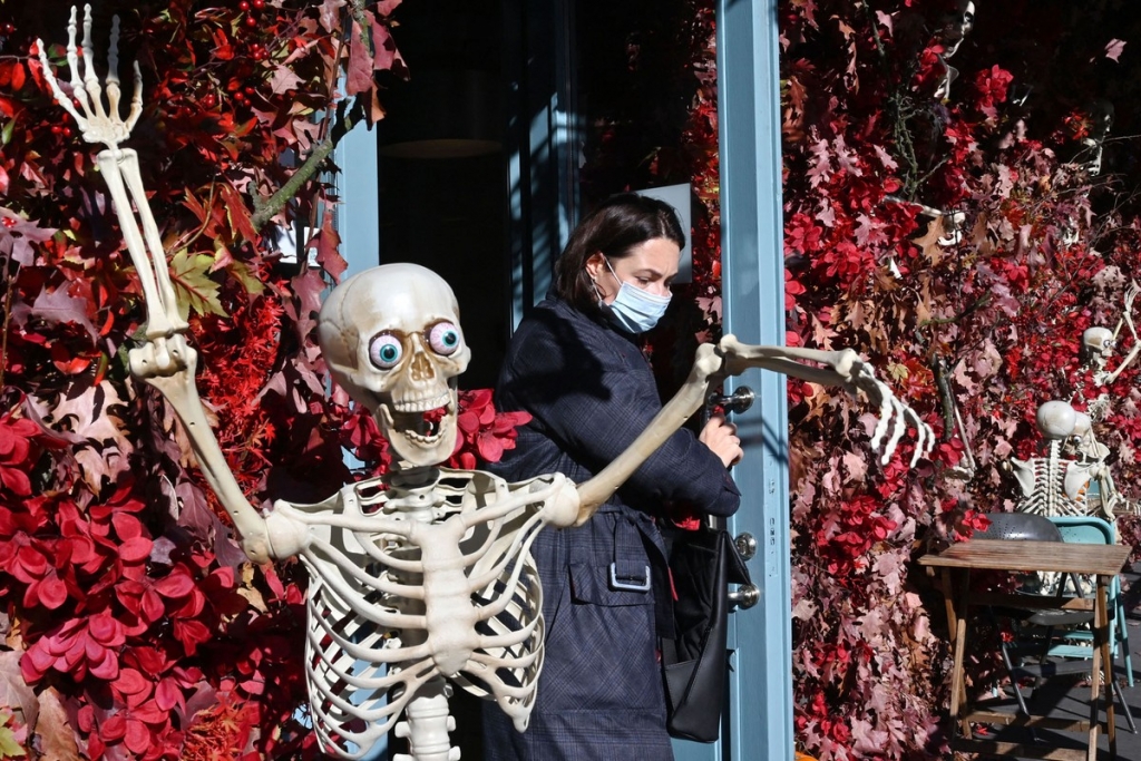 Một phụ nữ đeo khẩu trang rời một nhà hàng trang trí Halloween với một bộ xương ở Kiev, Ukraine, ngày 26/10. Ảnh: AFP.