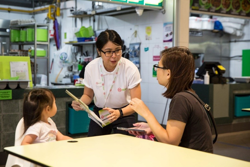 Một đại sứ giãn cách xã hội tại Singapore tuyên truyền thông tin cho thực khách tại một cửa hàng ăn uống bình dân