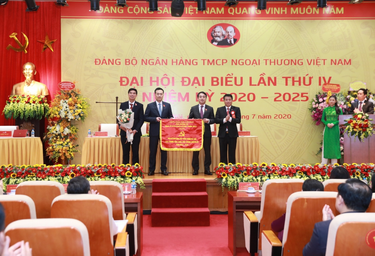 Đồng chí Y Thanh Hà Niê Kđăm - Ủy viên Dự khuyết Ban Chấp hành Trung ương Đảng, Bí thư Đảng ủy Khối DNTƯ (bên phải) trao Cờ thi đua cho Đảng bộ Vietcombank - đơn vị “đạt thành tích xuất sắc nhiệm kỳ 2015-2020”