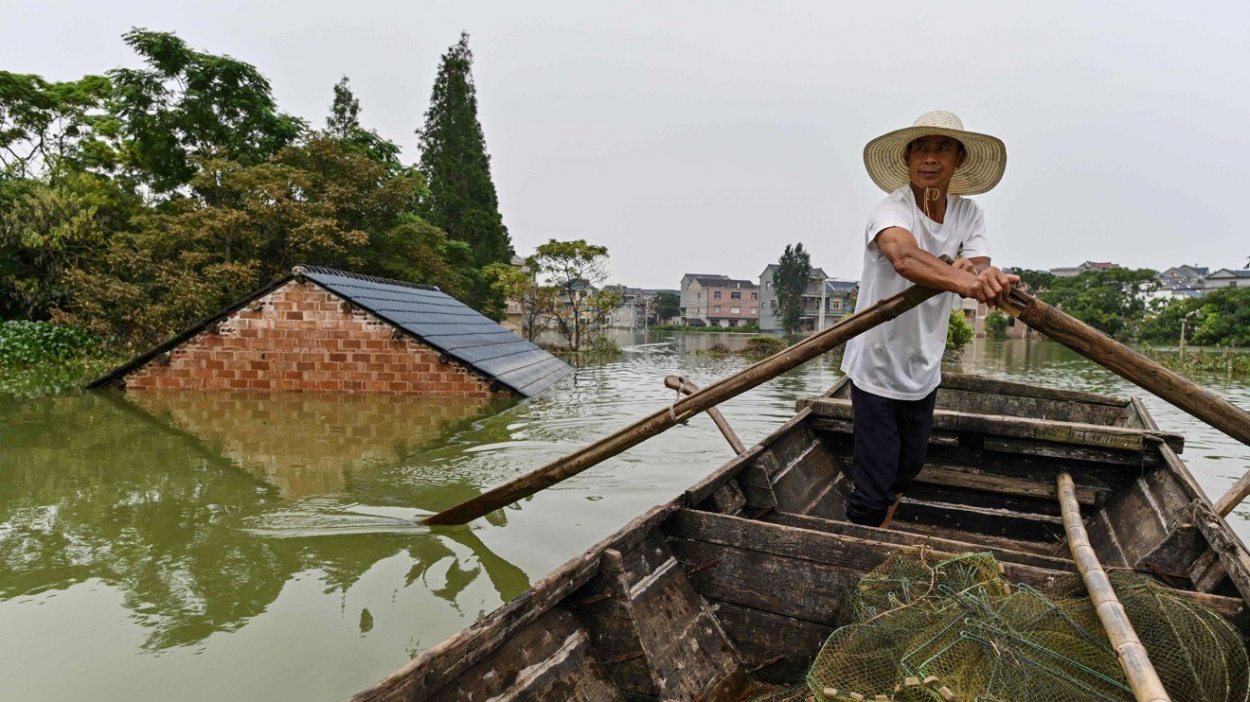 Người đàn ông đang chèo thuyền qua một ngôi nhà ngập nước ở làng Long Khẩu, Giang Tây (Ảnh: AFP)