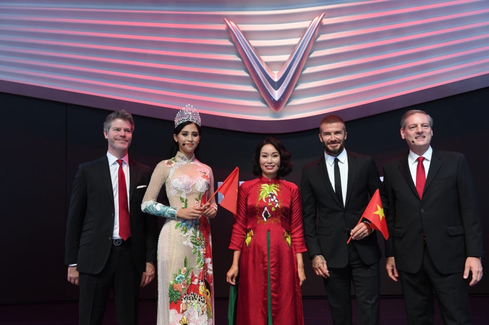Tiểu Vy và David Beckham chụp ảnh lưu niệm cùng  Ban lãnh đạo của VinFast. Từ trái qua phải: ông Dave Lyon - Giám đốc thiết kế của VinFast, Hoa hậu Tiểu Vy, bà Lê Thị Thu Thuỷ - Phó Chủ tịch Tập đoàn Vingroup kiêm Chủ tịch VinFast, ông James Deluca - Tổng giám đốc nhà máy VinFast.