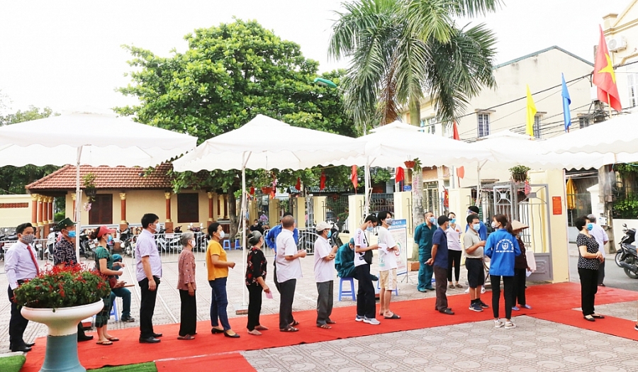 Các cử tri xếp hàng, thực hiện sát khuẩn tay trước khi vào khu vực bỏ phiếu